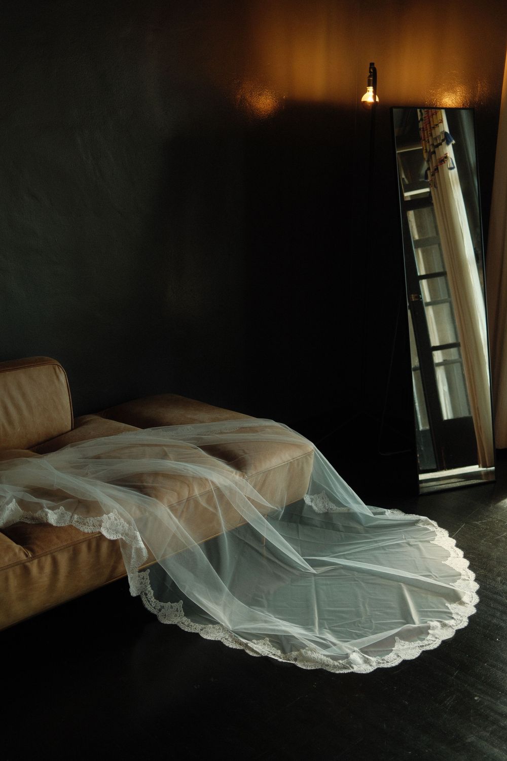 Elegant bridal veil draped over a leather chaise lounge in a dimly lit wedding suite.