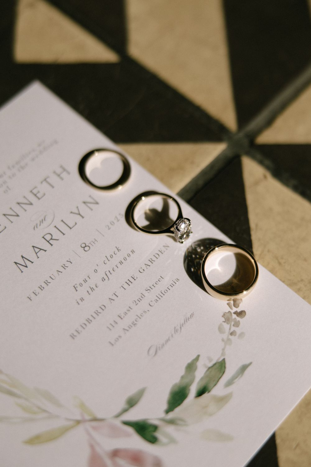 Wedding rings and diamond engagement ring displayed on elegant floral wedding invitation.