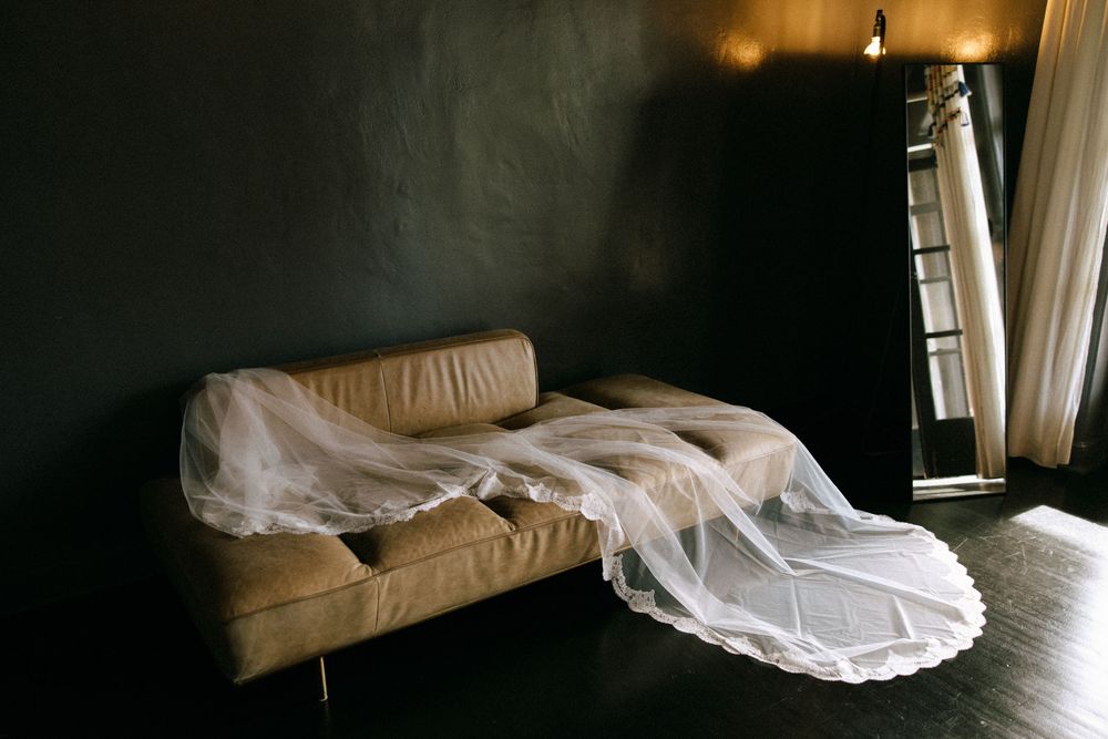 Bridal veil draped over leather sofa in dark moody hotel room before wedding.