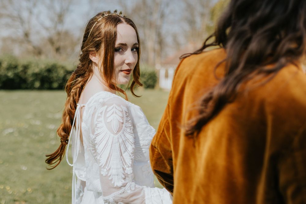 Woman in white lace wedding dress smiles over shoulder while standing near someone in autumn outdoor setting.