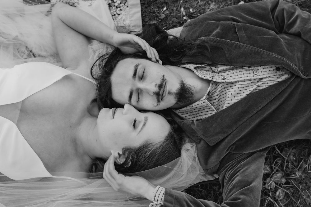 A romantic black and white close up photo of a couple lying together on grass with their heads touching.