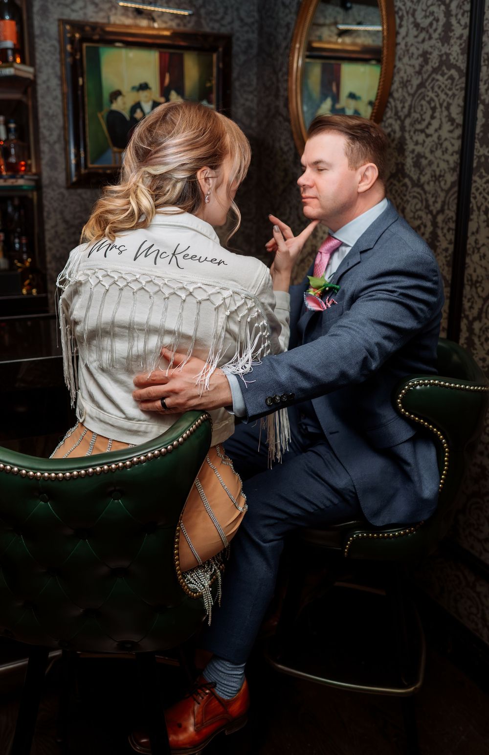 A couple in formal attire shares a playful moment on vintage furniture.