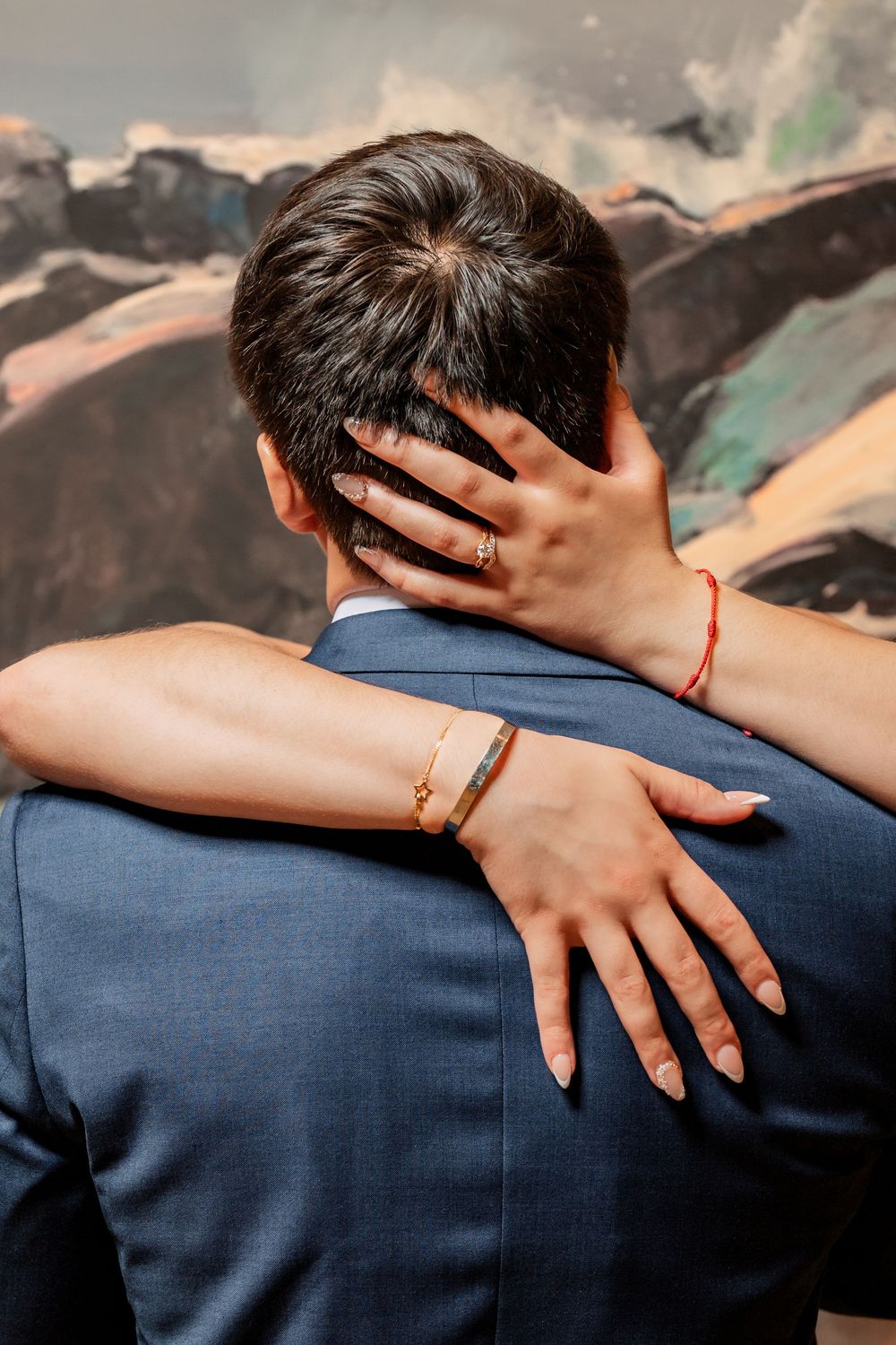 Close-up of hands embracing across blue suit jacket.