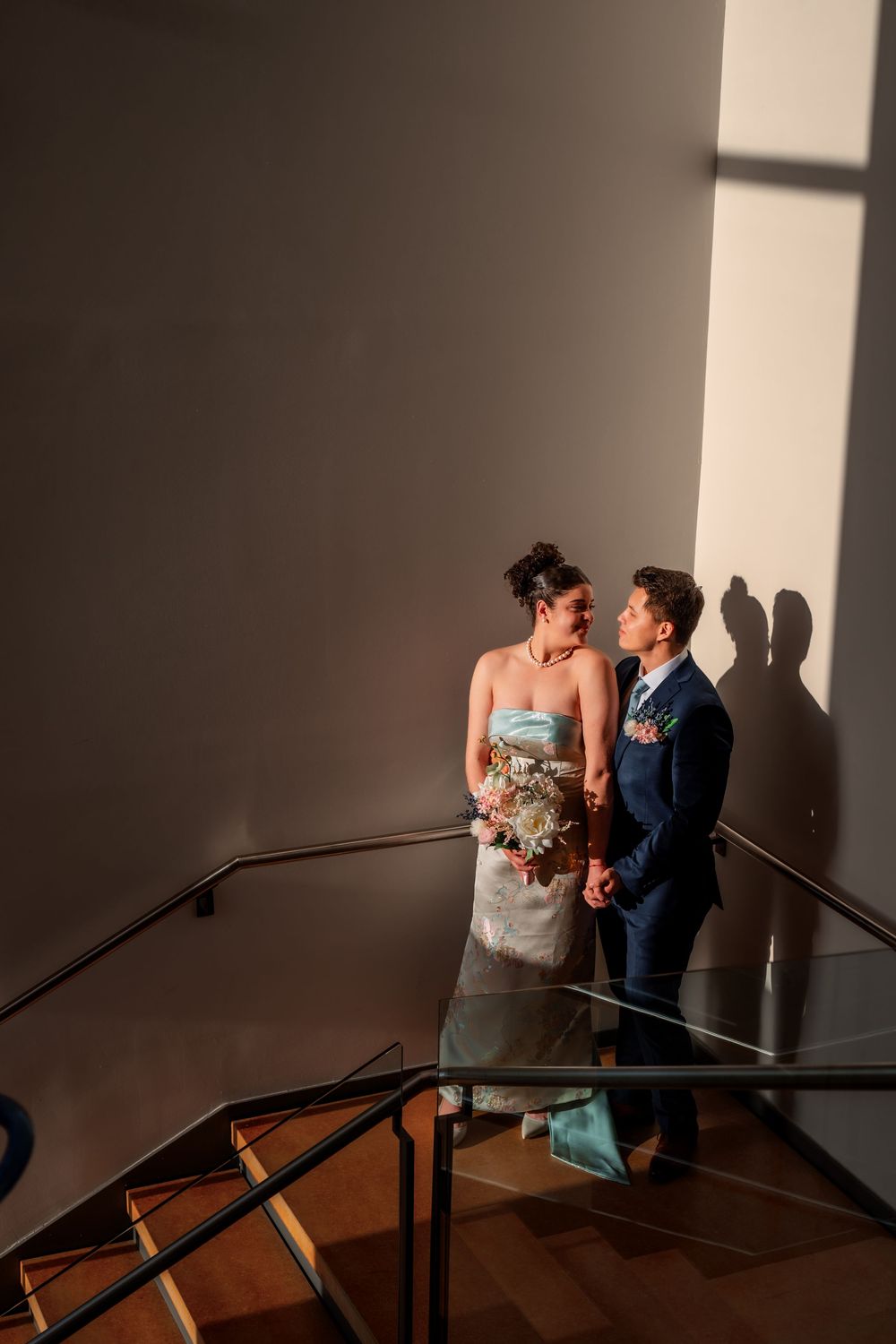 A romantic couple shares an intimate moment in dramatic lighting against a dark wall with shadows.