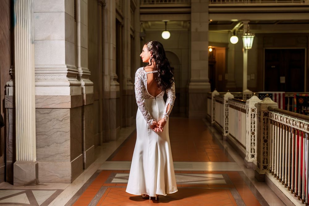 A bride in a long white dress poses in an elegant hallway with classical architecture.