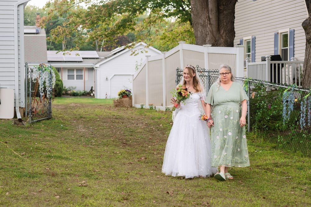 Wedding party poses for photos on a grassy lawn with white houses in background.