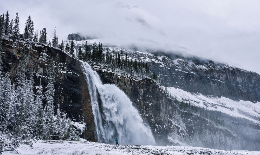 Massive waterfall cascading down snow-covered cliffs in winter landscape.