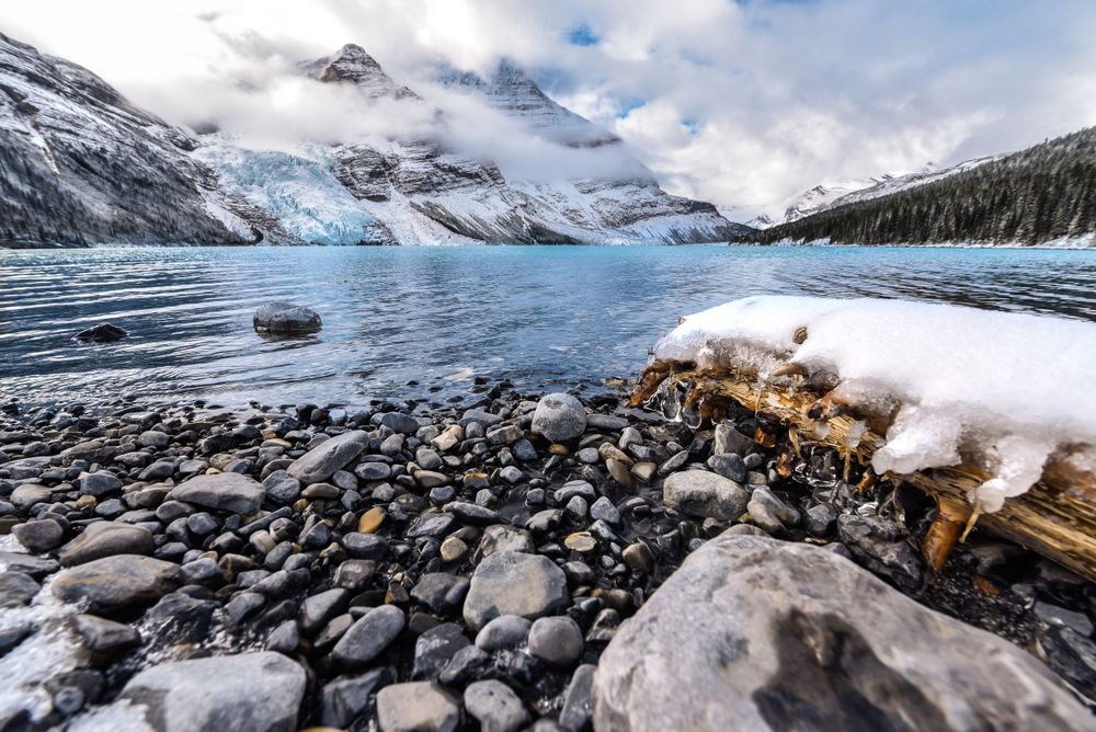 Winter scene of frozen lake with rocky shore and snow-covered mountain peaks.
