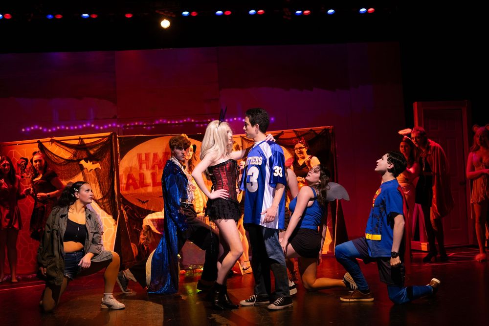 Cast members perform an intense dramatic scene in colorful costumes during a musical theater production.