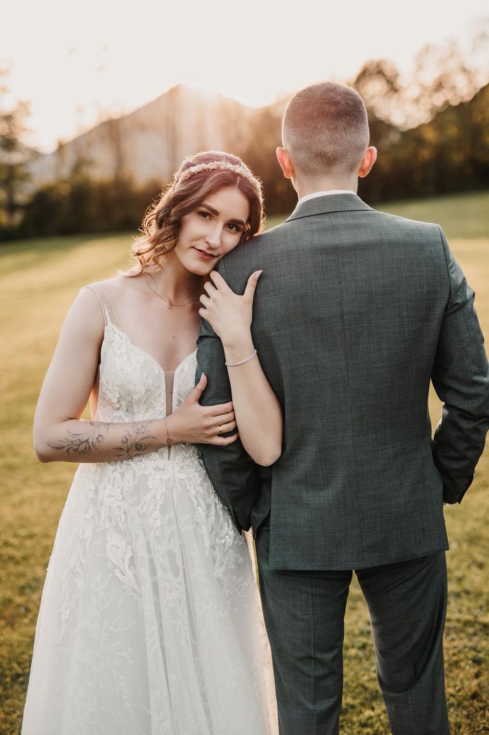 Bride in lace gown and groom in grey suit share intimate moments during golden hour.