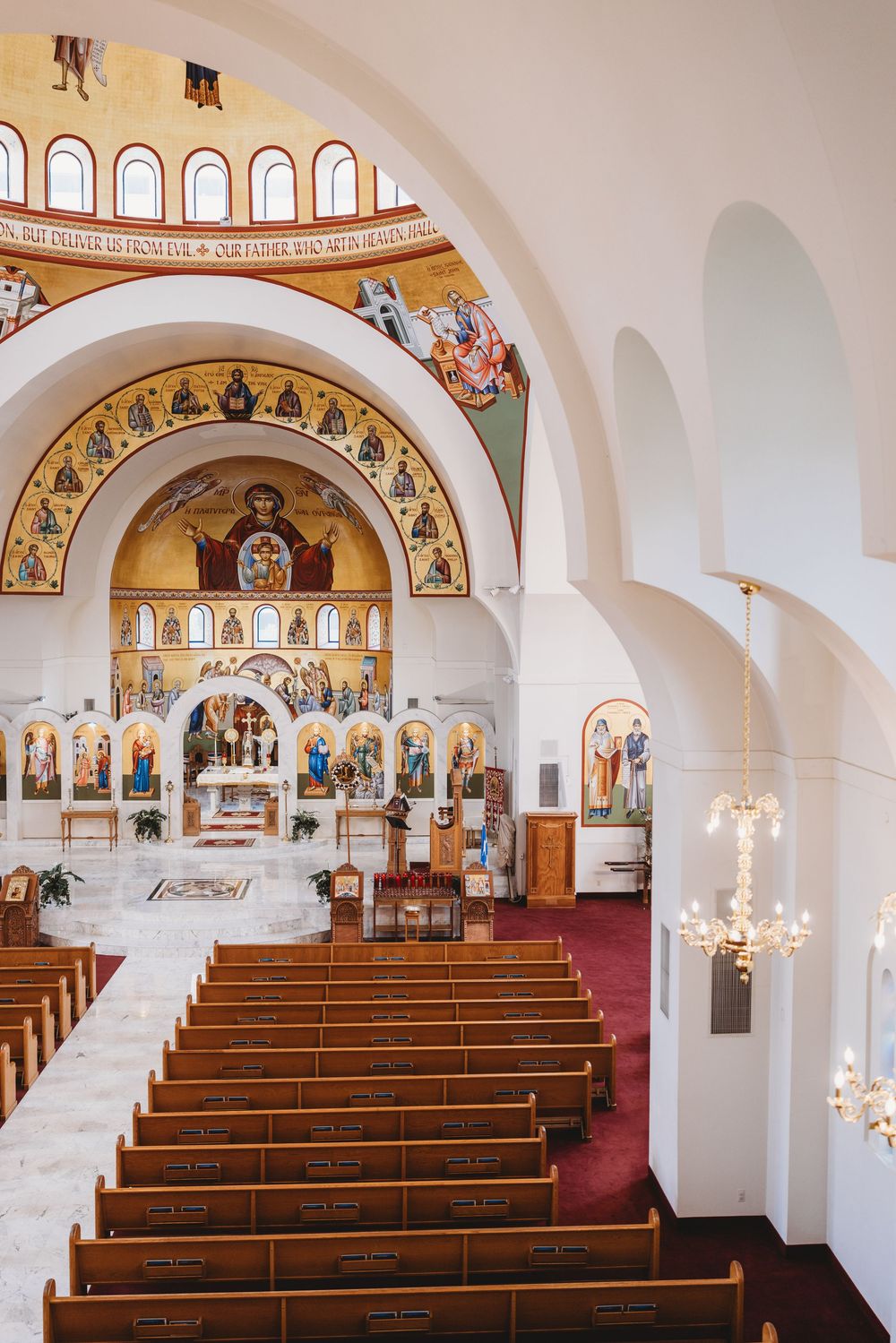Interior of an ornate church with wooden pews and Byzantine-style religious artwork adorning the walls and ceiling.