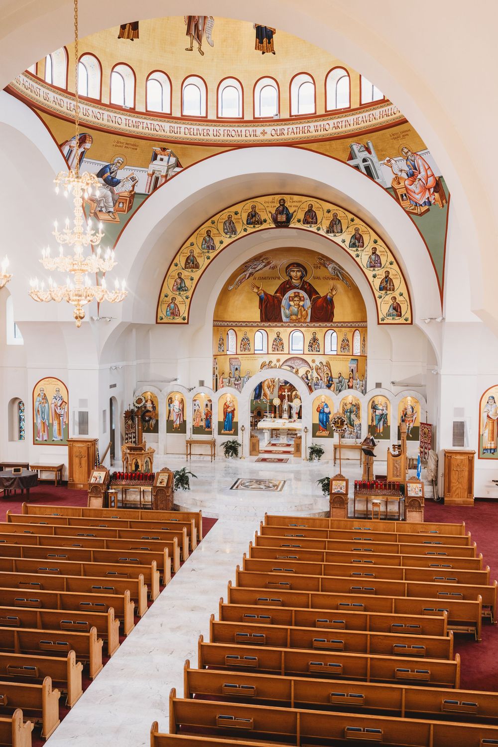 Interior view of an Orthodox church with ornate frescoes, chandeliers and wooden pews.