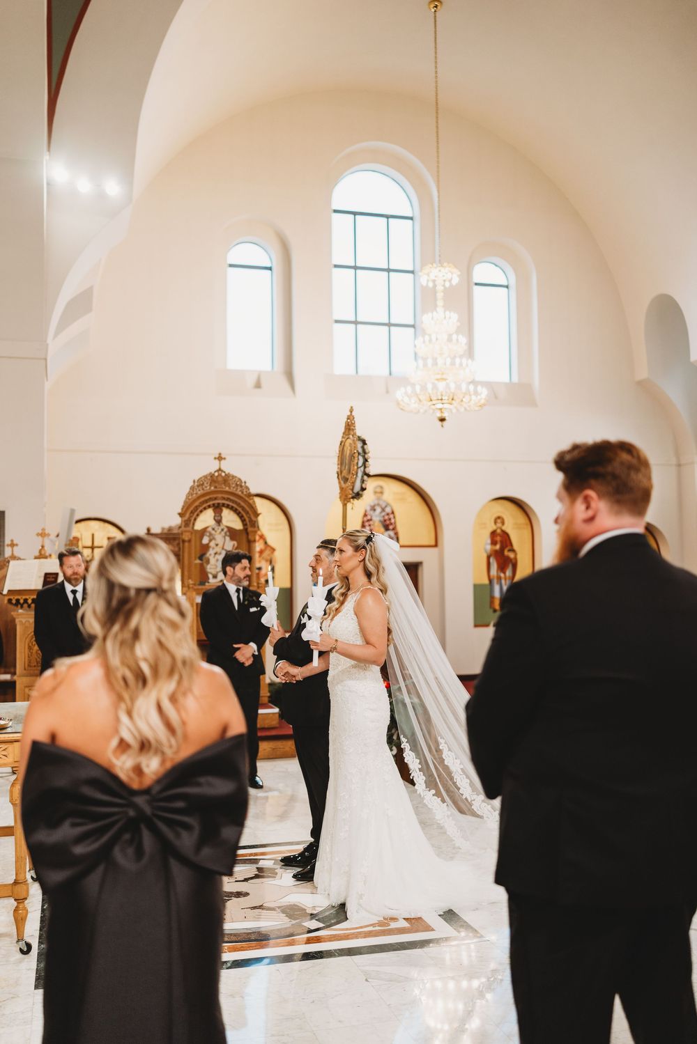 Wedding party celebrates with a first look reveal in a bright white church with arched windows and elegant chandeliers.