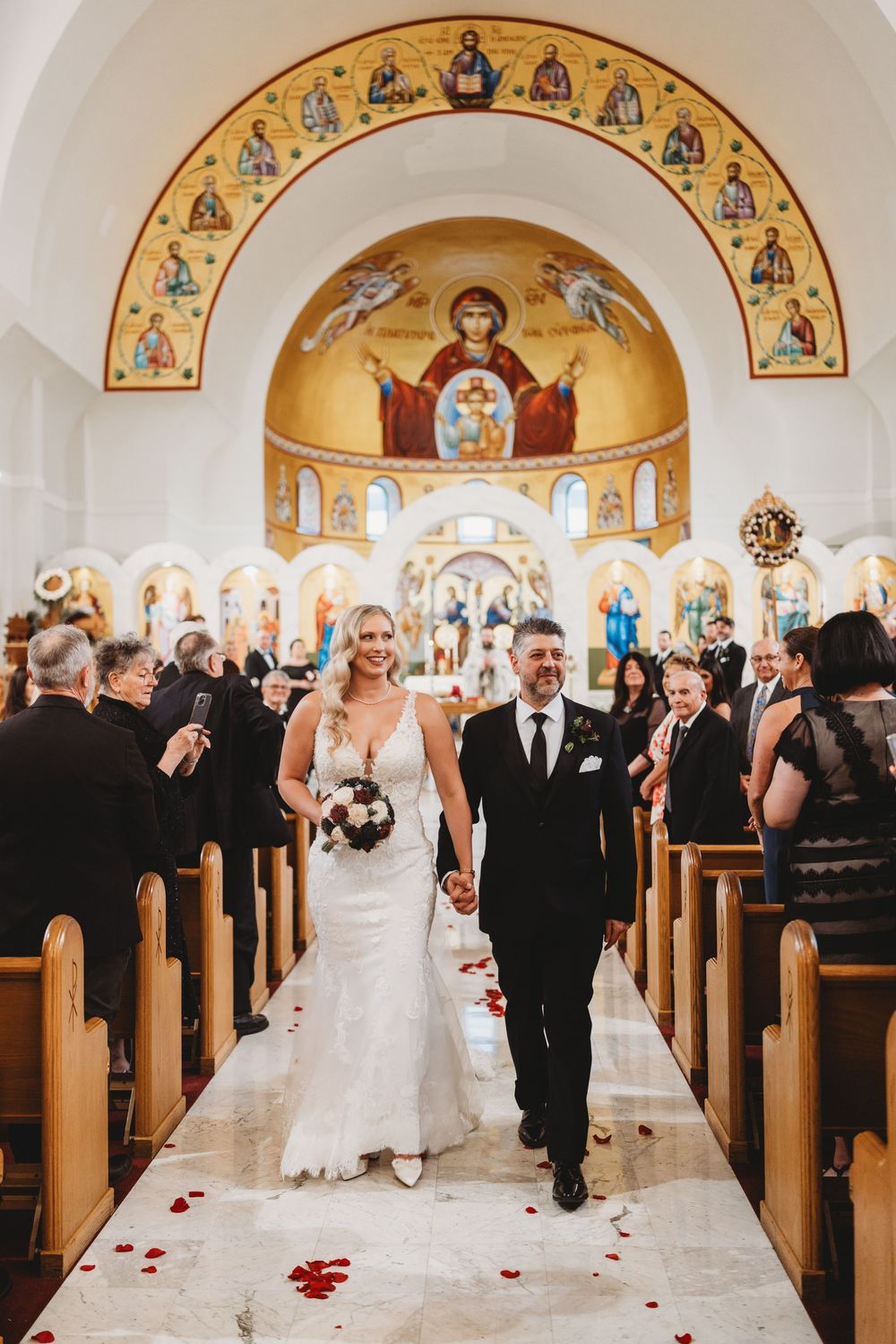 Wedding ceremony in a Byzantine-style church with guests raising their hands in celebration.