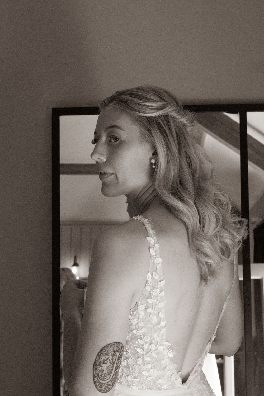 Black and white portrait of bride in backless lace gown with tattoo visible.
