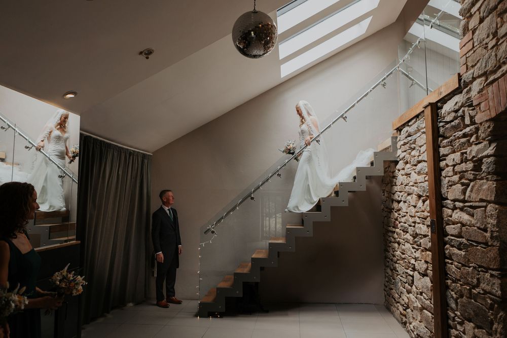 Bride descending modern staircase as groom waits below in elegant wedding venue.