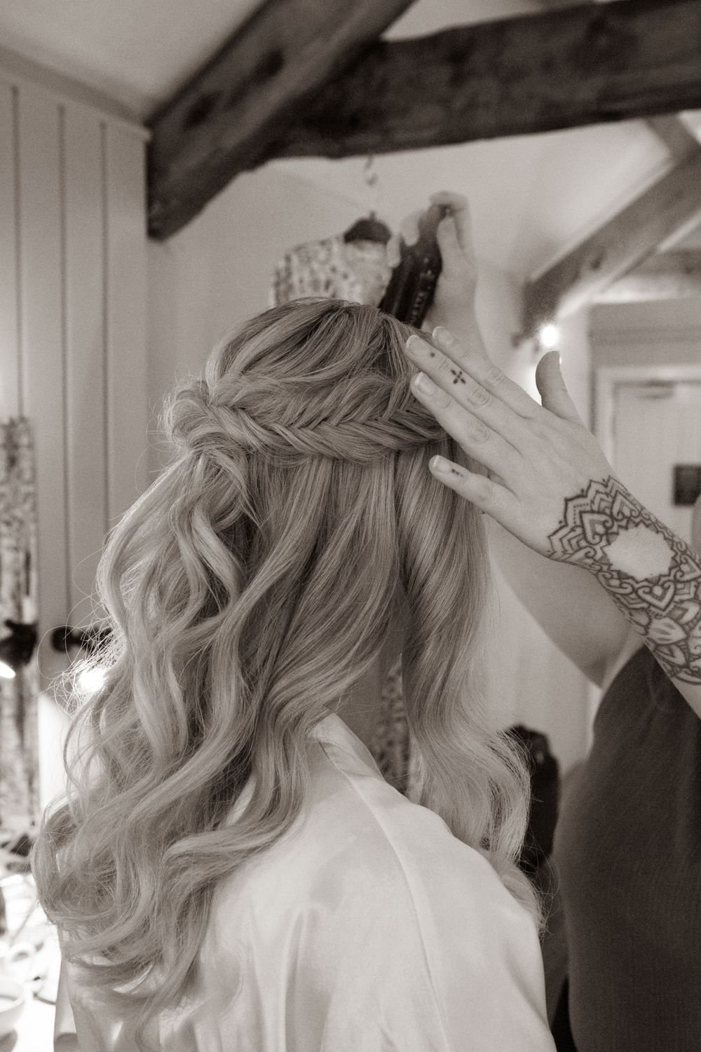 Black and white photo of bride's elegant half-up wavy hairstyle with braid detail during wedding prep.