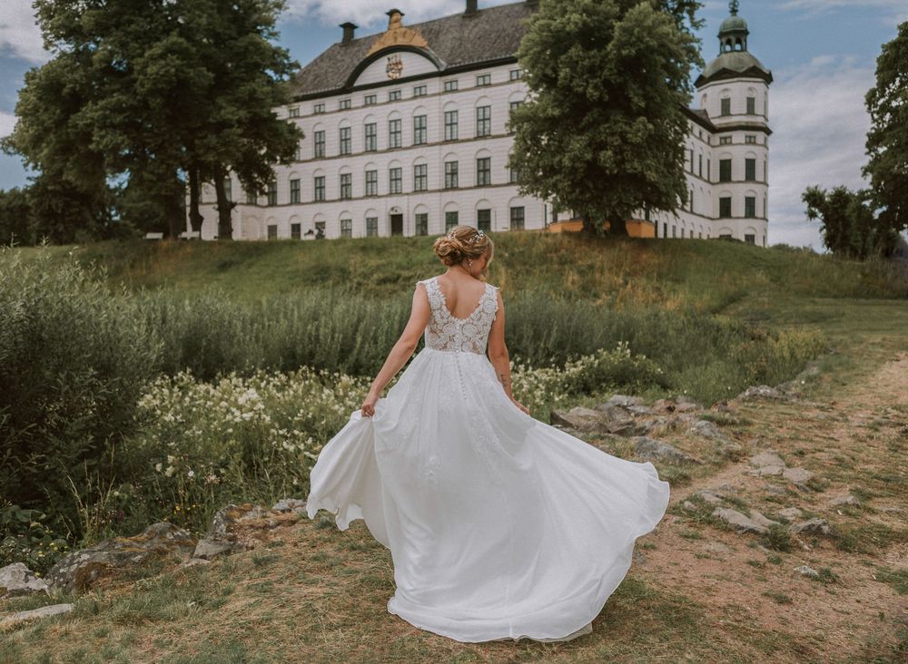 Bride twirling in white lace gown on path before a grand Swedish castle.