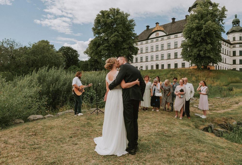 Couple sharing first kiss at outdoor wedding ceremony before a Swedish castle.