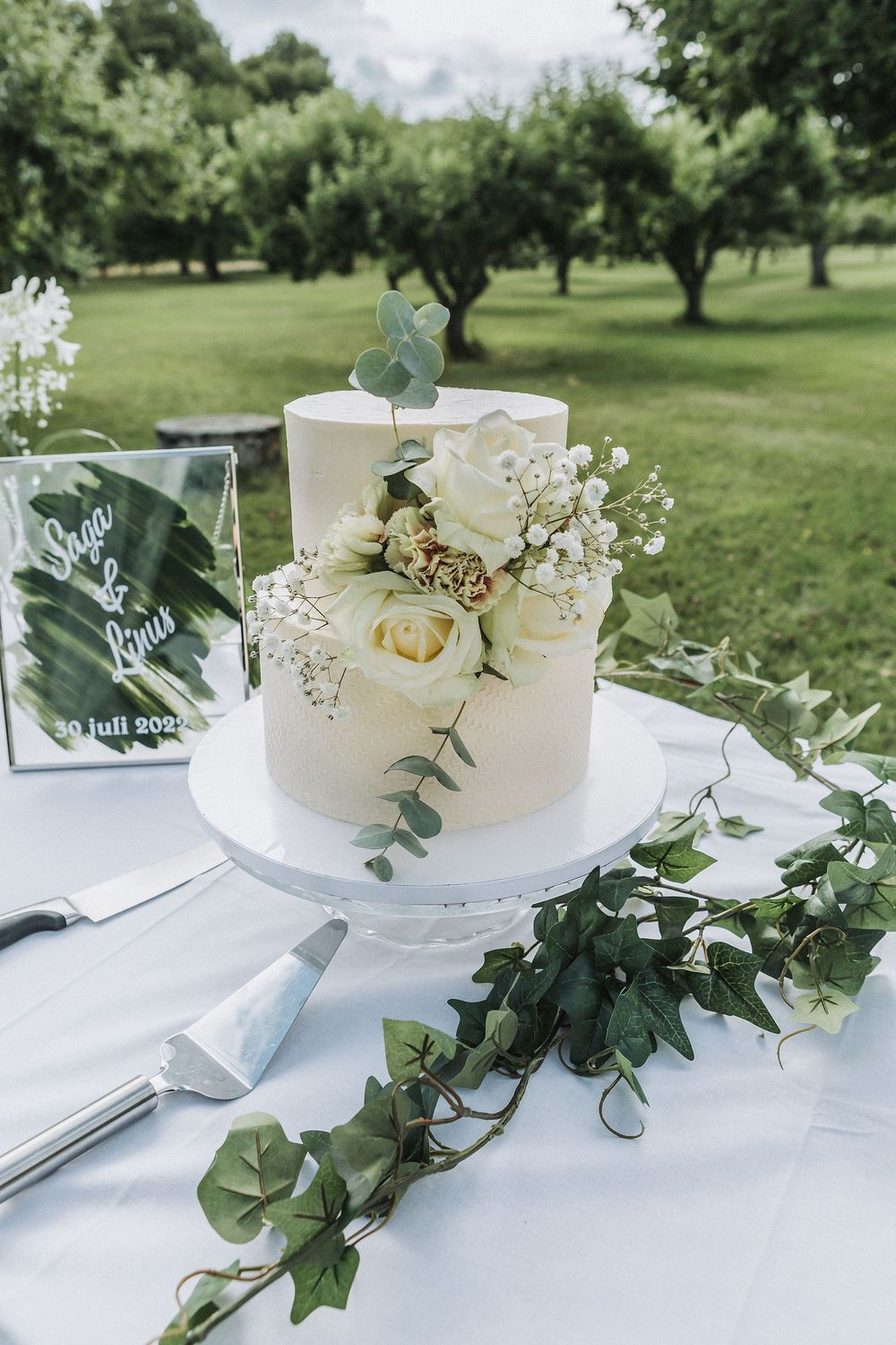 Elegant two-tier white wedding cake adorned with roses and eucalyptus outdoors.