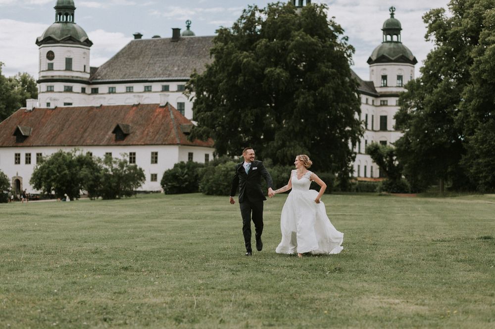 Bride and groom walking hand in hand across green lawn before a grand castle.