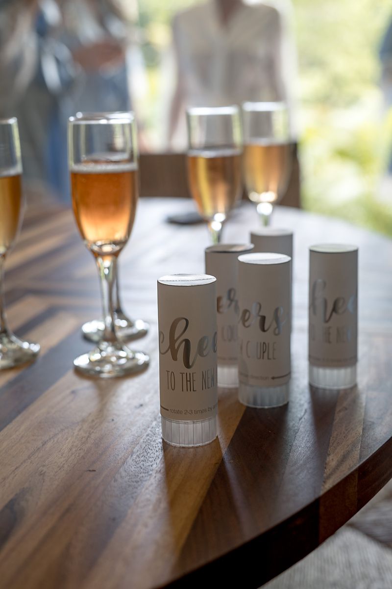Champagne flutes and white party favor tubes with gold lettering arranged on a wooden table at a celebration.