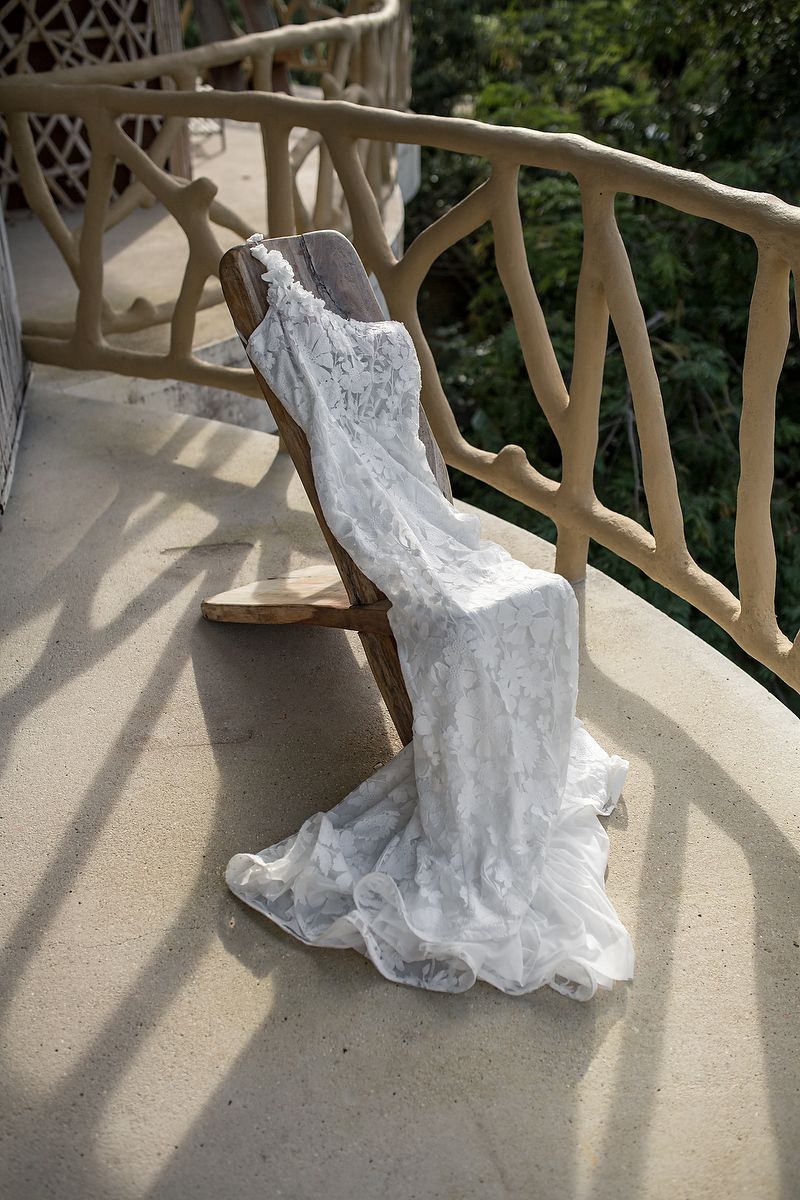 A white wedding dress train cascades across a curved balcony with ornate railing details and dappled sunlight.