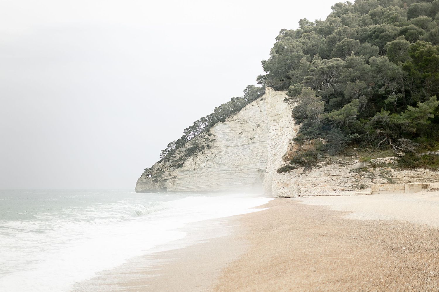 A scenic beach with rocky cliffs and lush green vegetation overlooking a sandy shoreline and blue ocean waters.