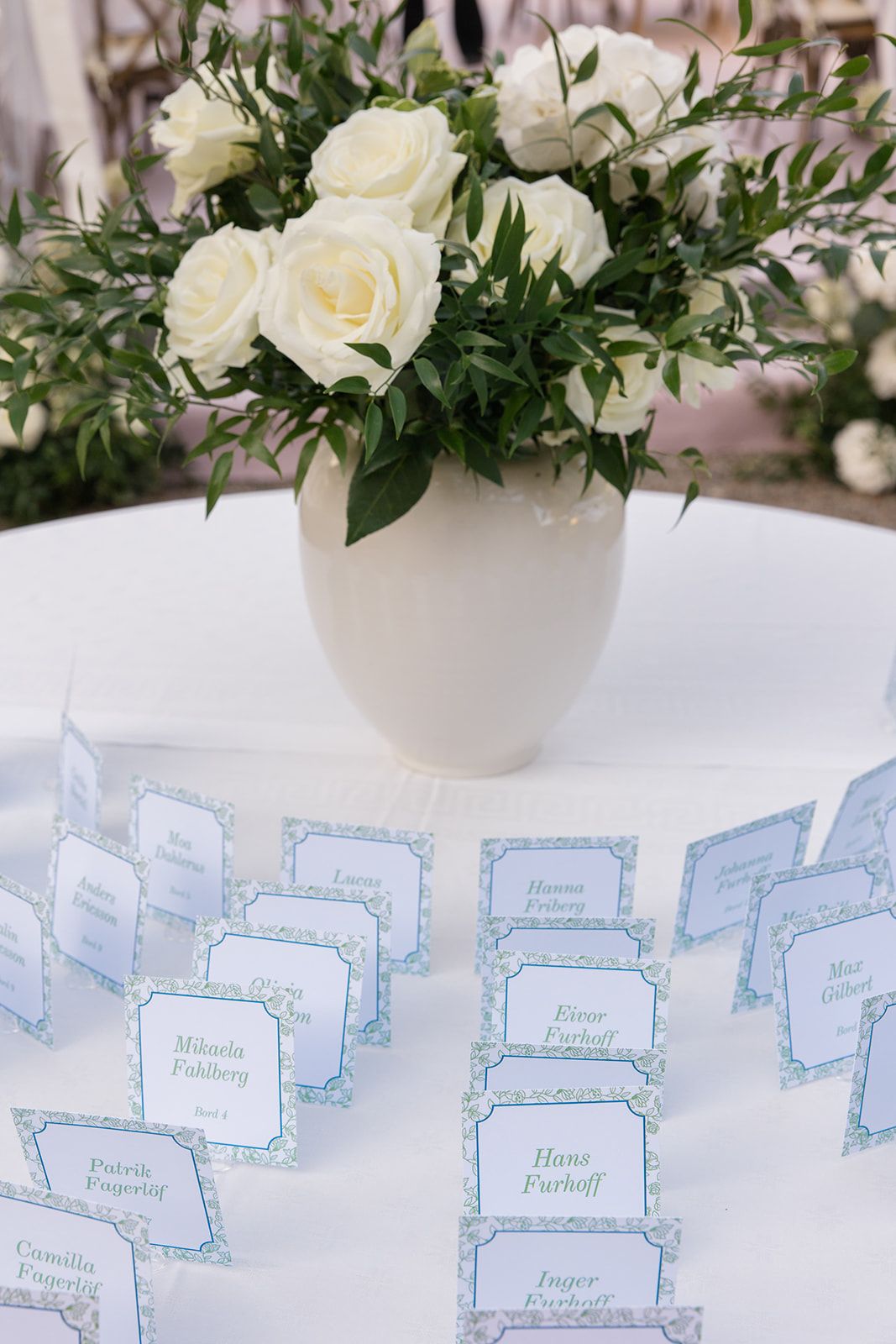 White floral centerpieces and elegant blue-trimmed place cards create a sophisticated wedding reception table setting.