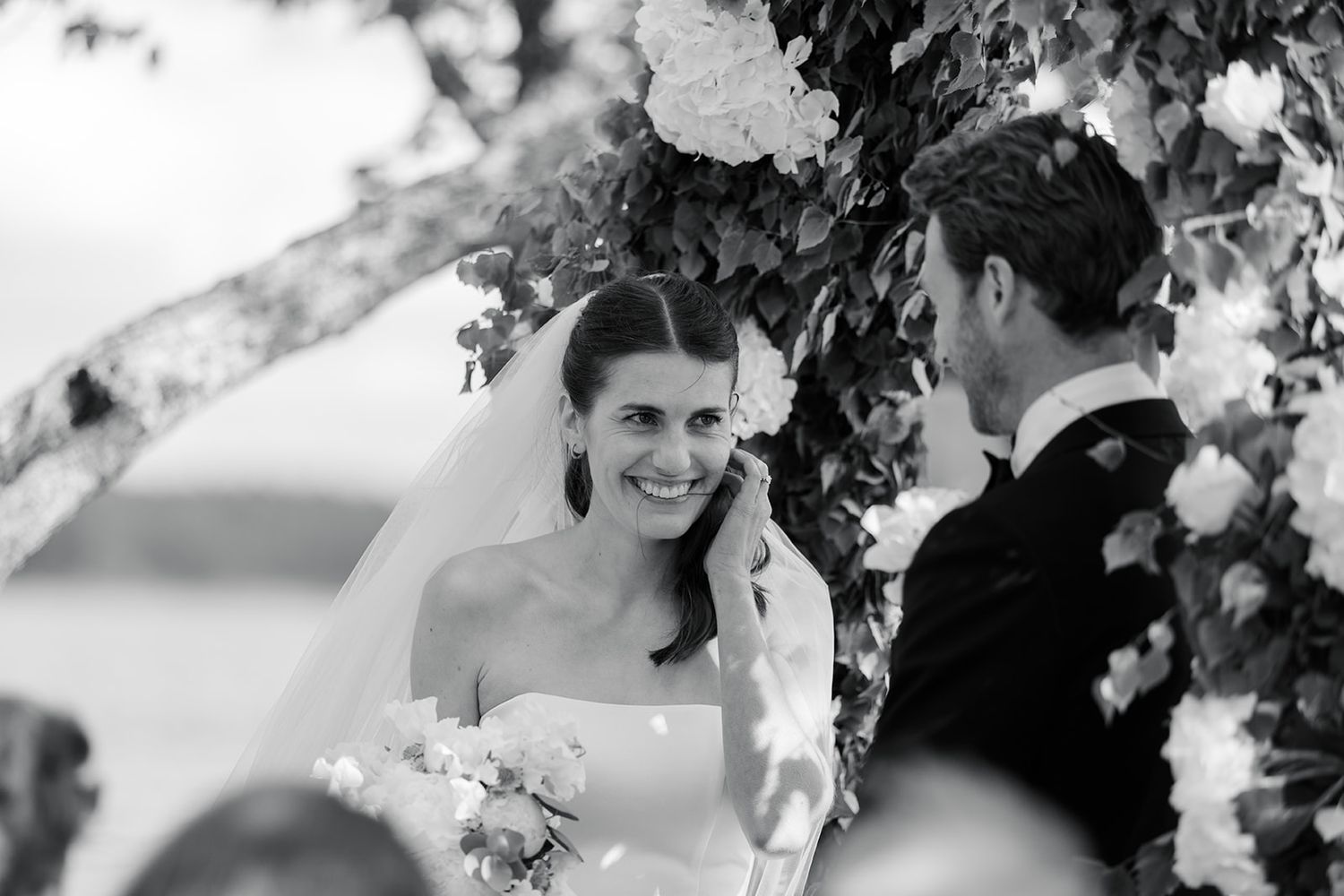 A romantic black and white wedding photo shows a couple embracing under flowering cherry blossoms.