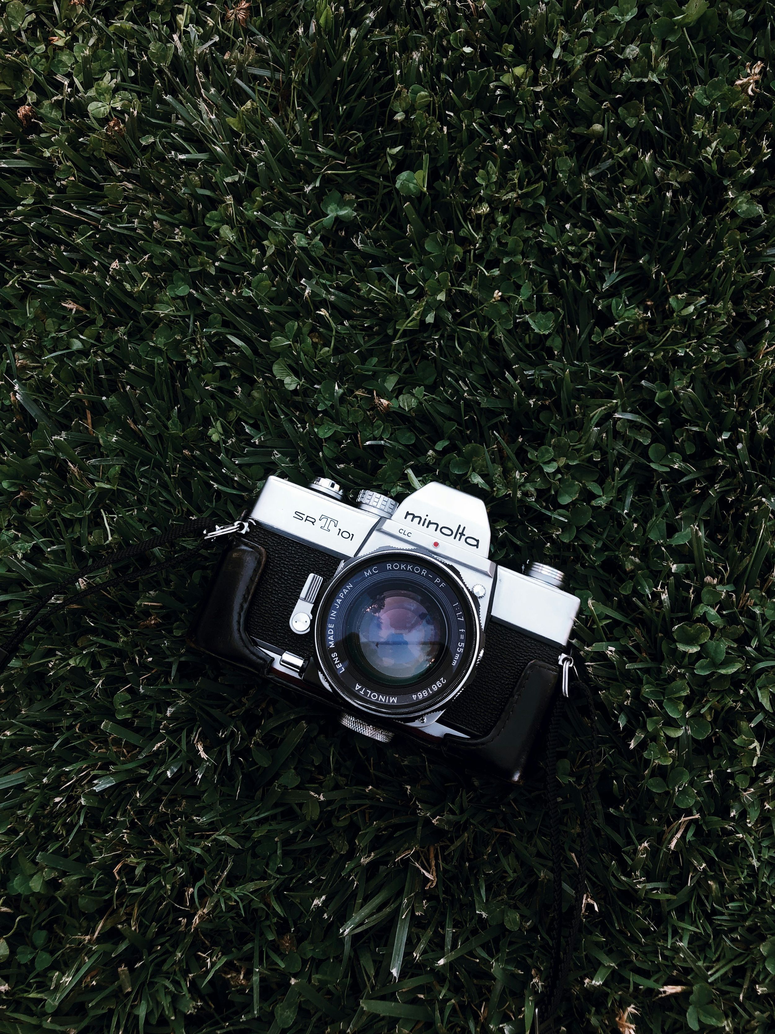 A vintage Minolta camera lying on green grass with a close-up view from different angles.