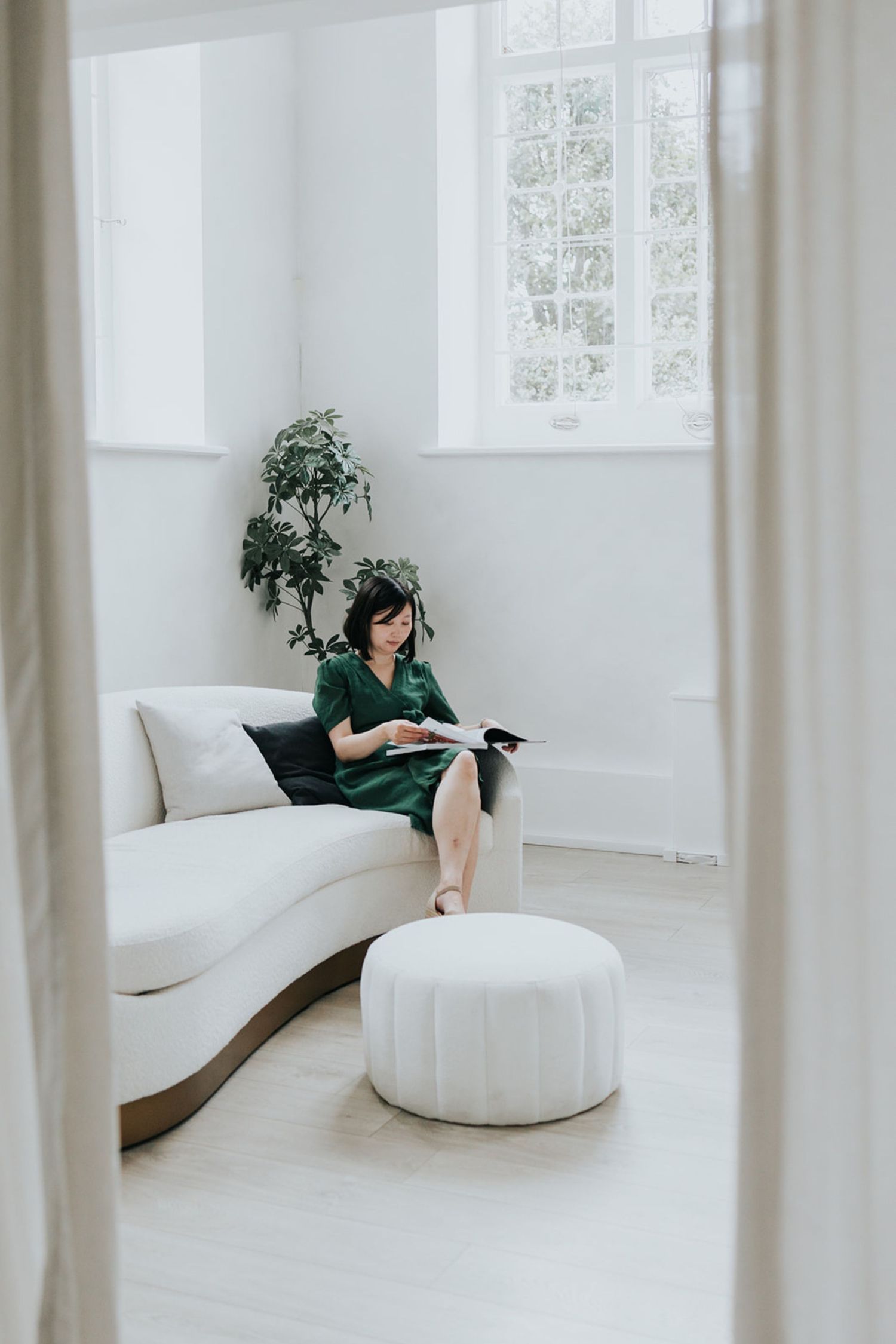 Woman in white sweater relaxes on couch in natural light while smiling at camera.