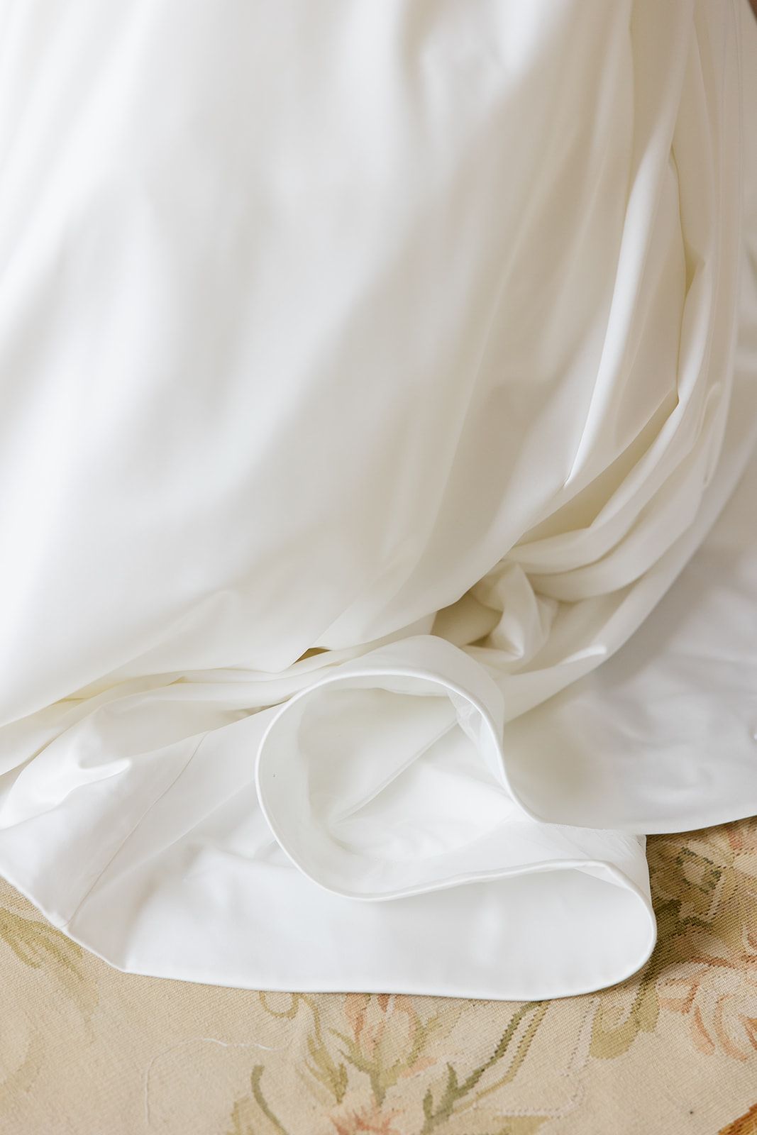Flowing white fabric drapes elegantly against a beige textured surface creating soft folds and shadows.