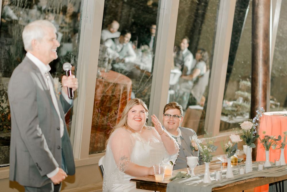 Wedding party members laugh and celebrate while toasting with drinks at an elegant indoor reception venue.