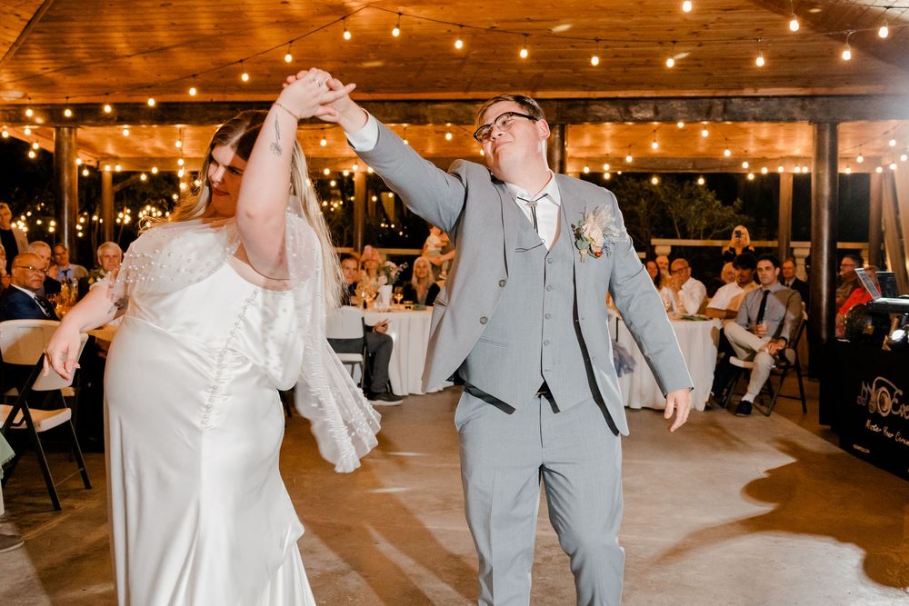 Wedding reception venue decorated with warm string lights and guests dancing on wooden floor.