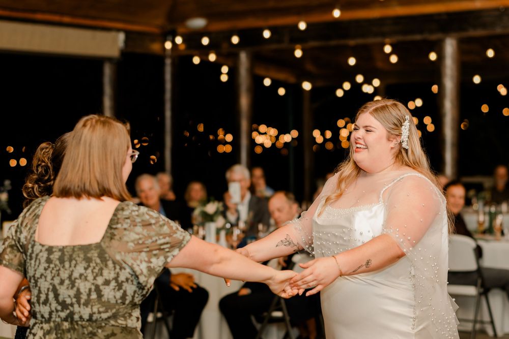 Wedding guests dance and celebrate on a dimly lit dance floor decorated with string lights above.