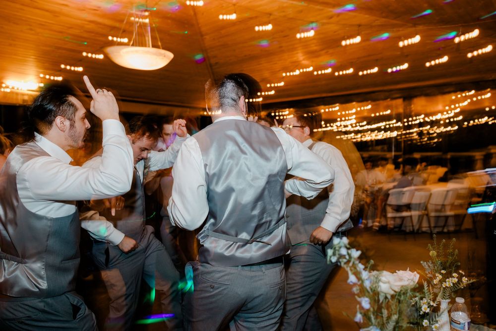 Couples dancing together on a wooden floor beneath string lights at an indoor wedding reception venue.