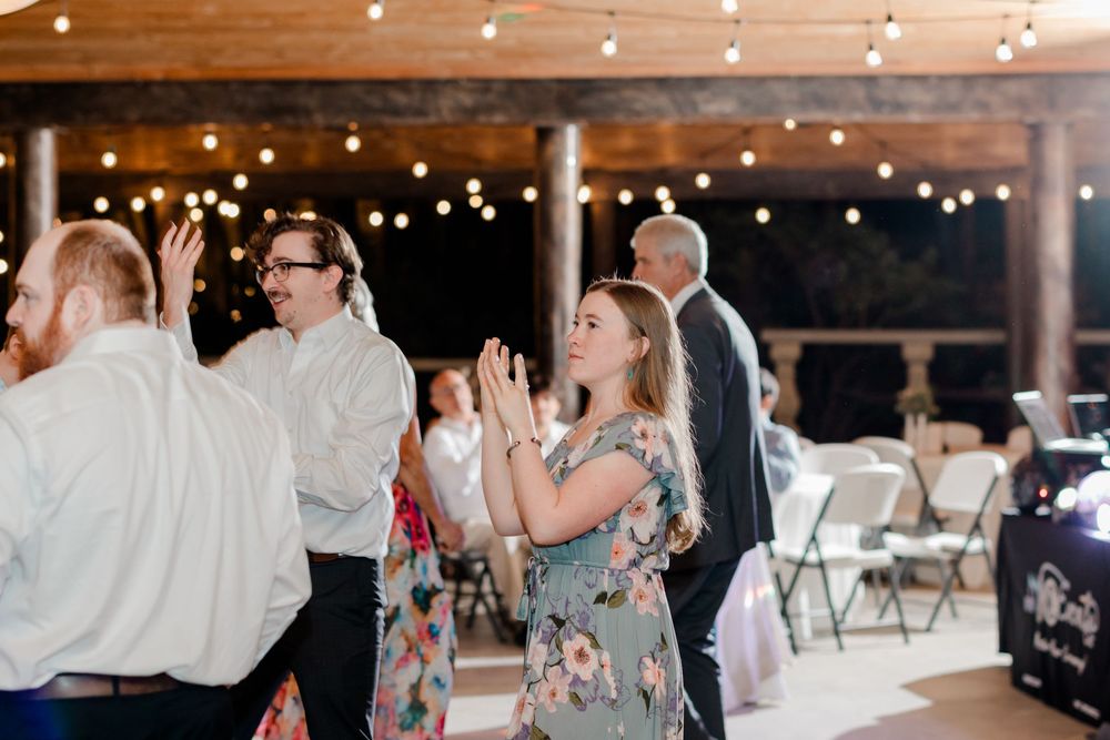 Wedding reception dance floor filled with guests enjoying themselves under twinkling lights in a rustic venue.