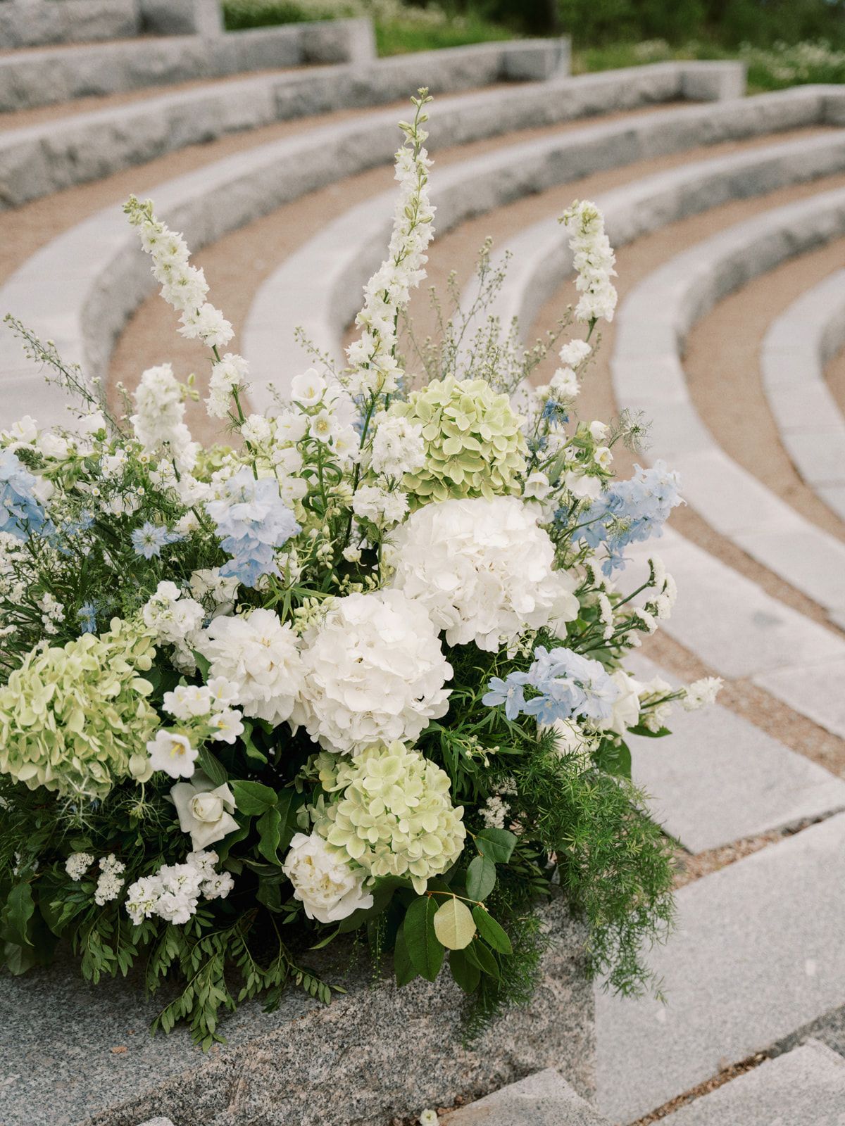White floral arrangements with delicate greenery line concrete steps in an elegant outdoor setting.