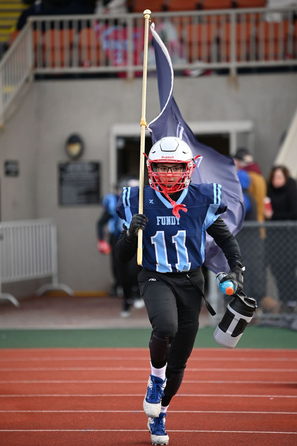 Four sequential action shots show a football player running on the field pregame carrying a flag.