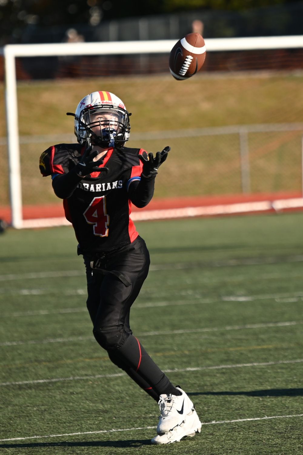 Football player in black uniform reaches to catch a spiraling football during a game on sunny field.