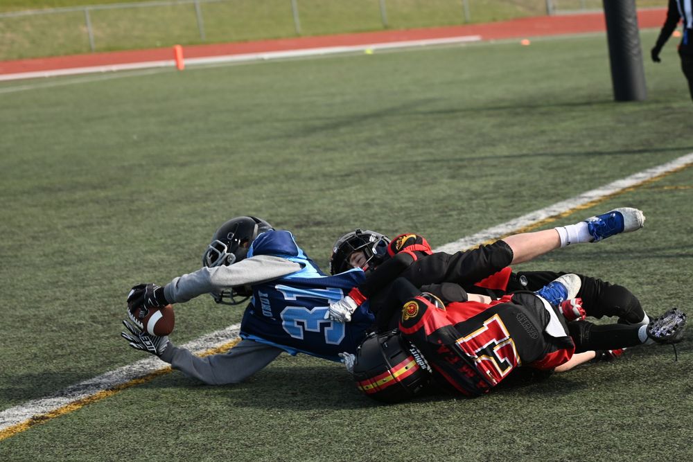 Football player stretches out for a touchdown while being tackled to the ground by the oposition.