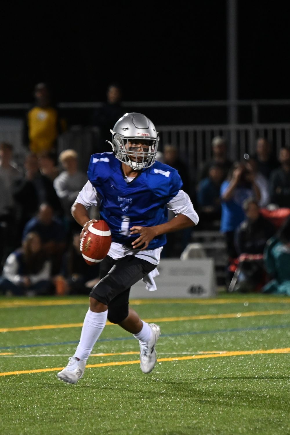 Football player in blue and white uniform dives to catch the ball during a night game on turf field.