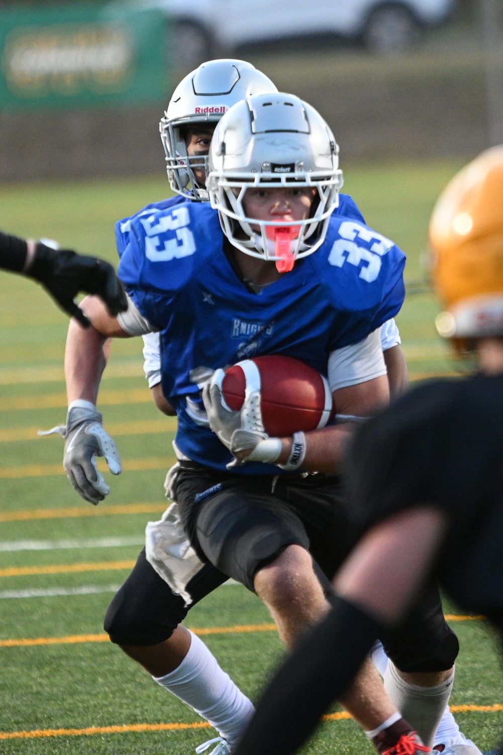 Football player in blue jersey number 13 carries ball during game on turf field.