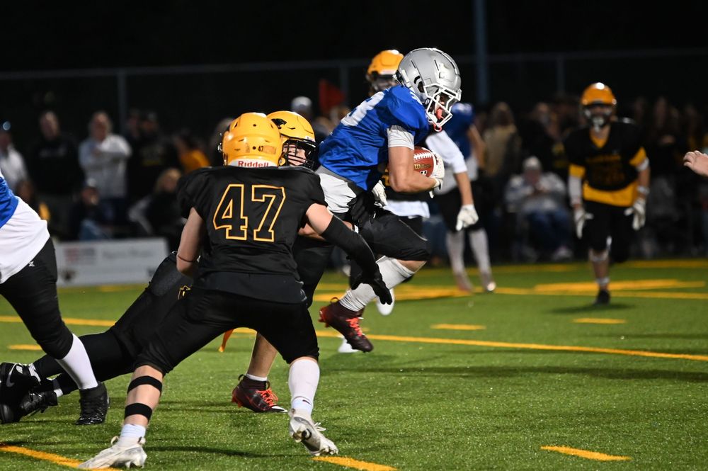 Football players in blue and yellow uniforms compete in an intense game on a brightly lit field at night.
