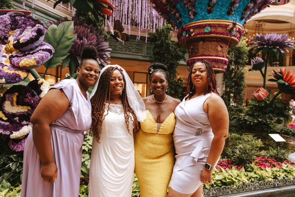 A group wearing white and yellow dresses celebrates joyfully in a garden setting.