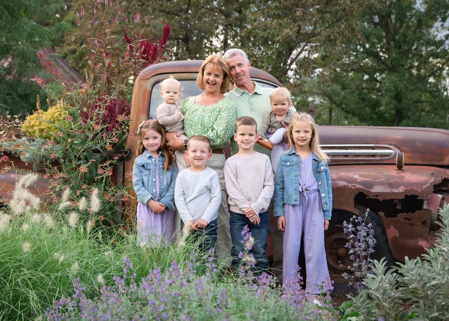 A group stands together outdoors wearing coordinated blue and lavender outfits for a family portrait session.