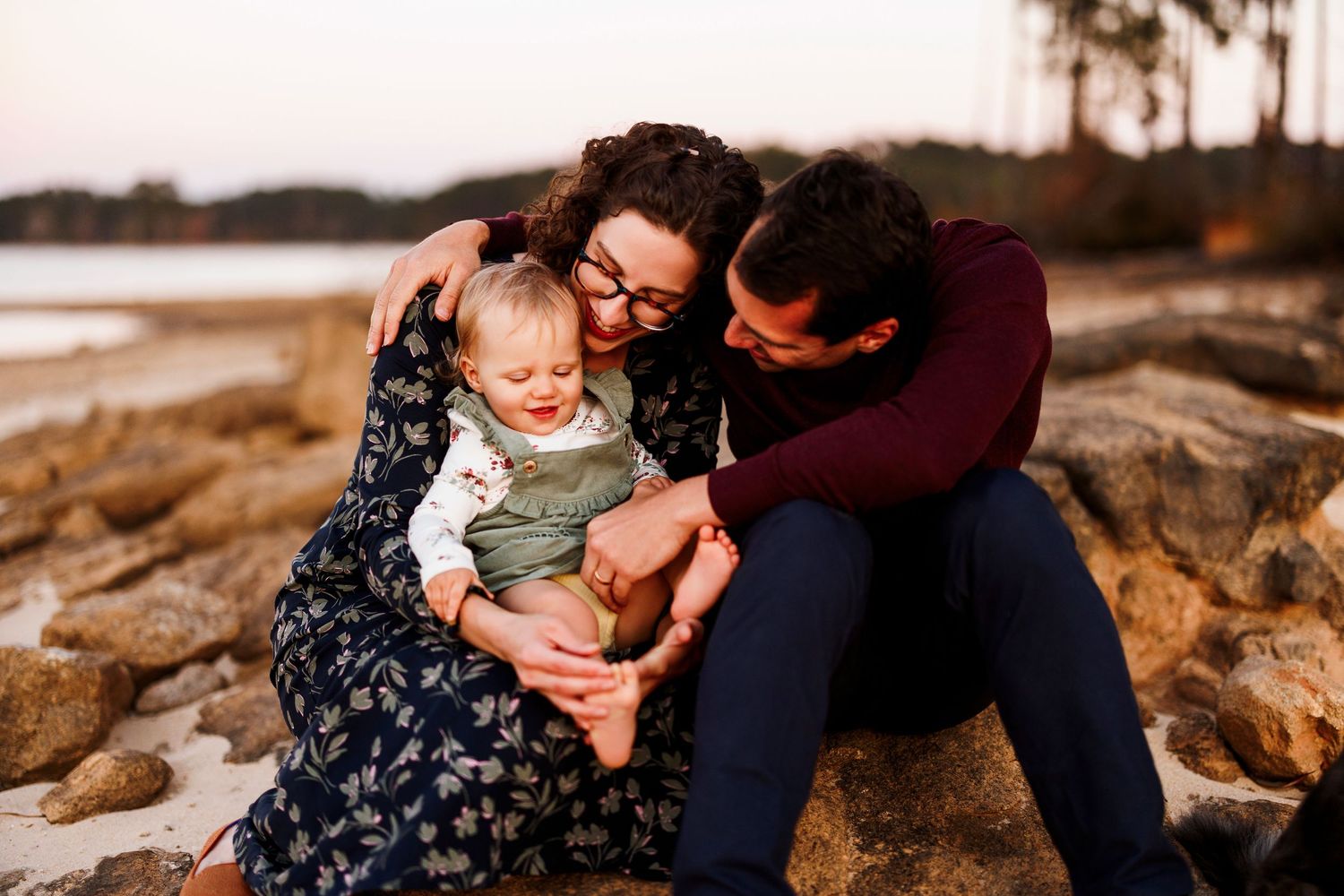 A family shares tender moments together during a sunset photoshoot on rocky coastal terrain.