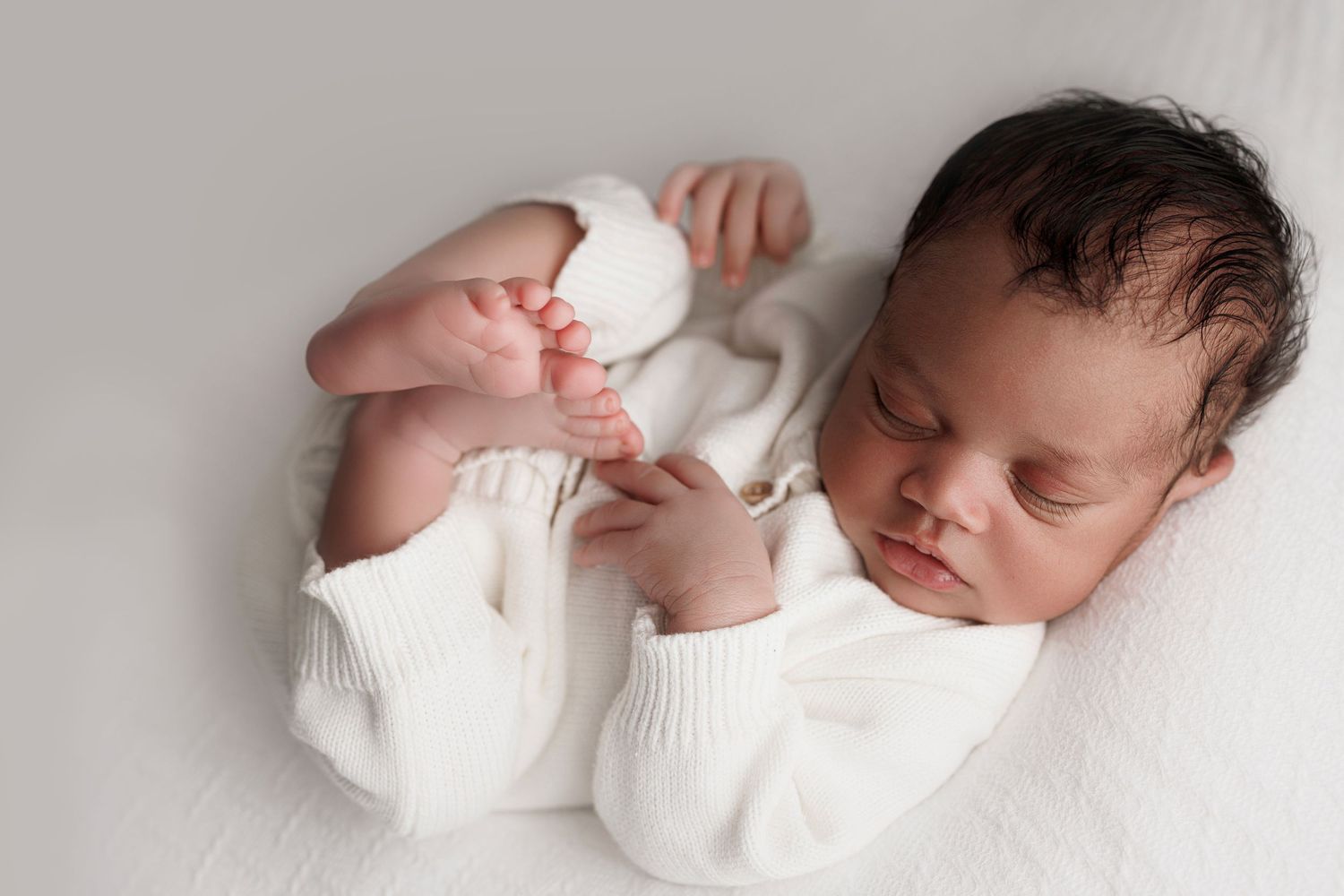A sleeping newborn baby wearing white clothing is shown in a series of four peaceful poses.
