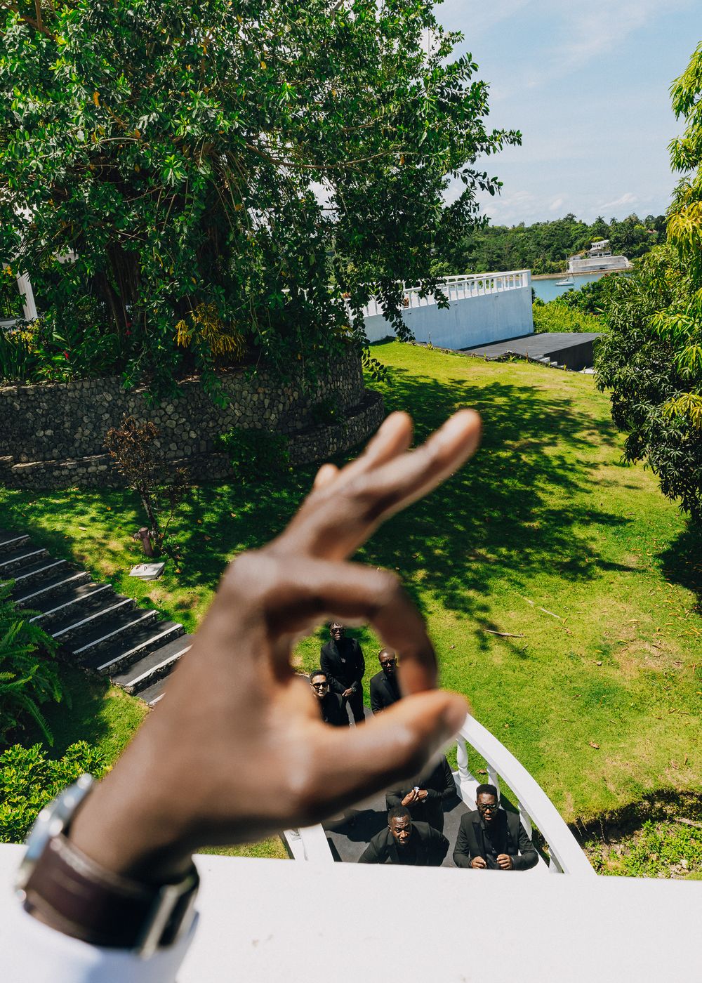 Hands gesturing against a sunny garden backdrop with green grass and trees.